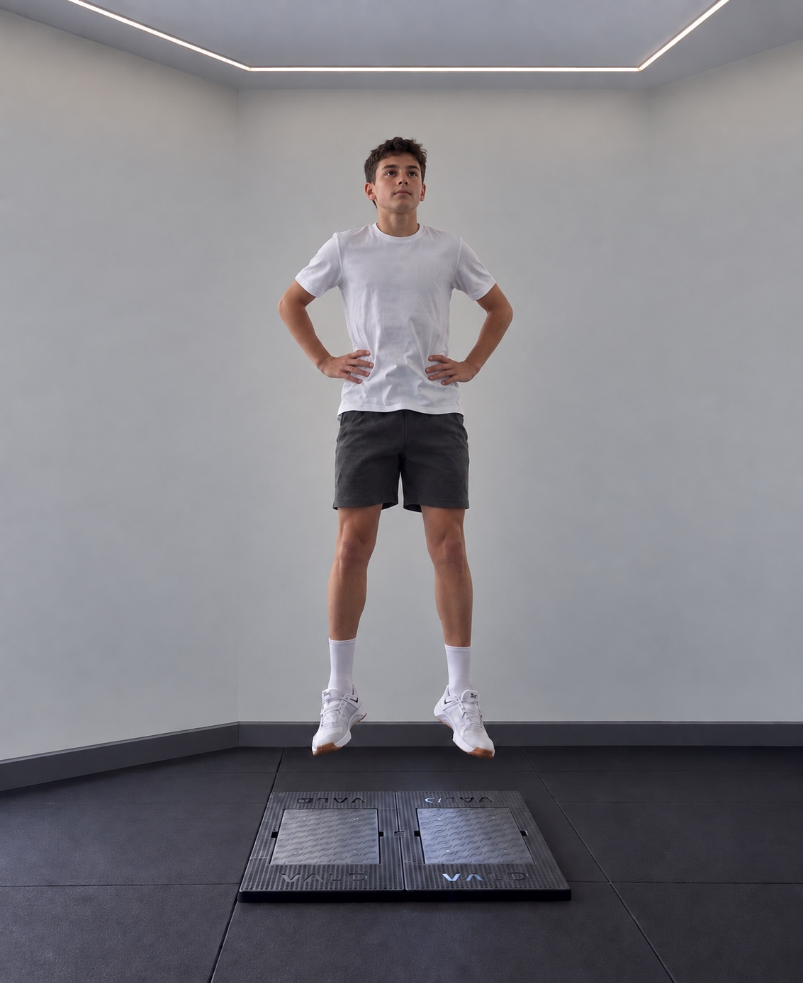 A youth athlete airborne above dual force plates with hands on hips during a countermovement jump